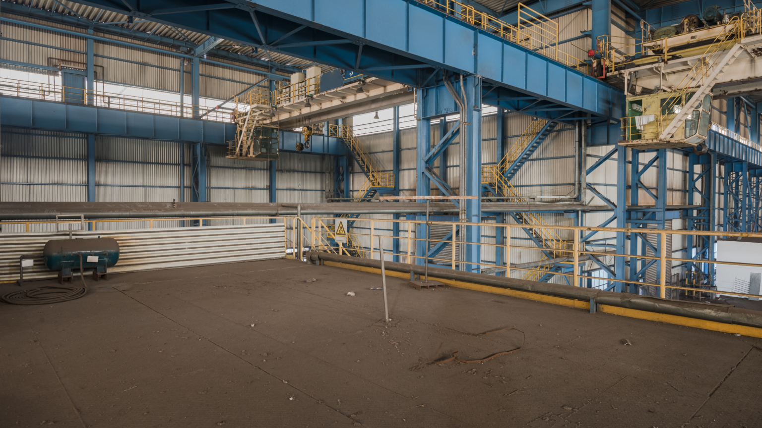 Grote industriële bedrijfshal met blauwe stalen spanten en kranen klaar voor onderhoud.