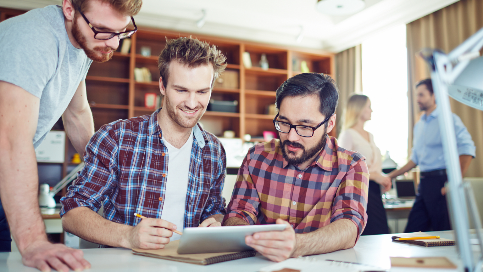 Drie collega's bekijken een tablet aan een bureau in een modern kantoor.