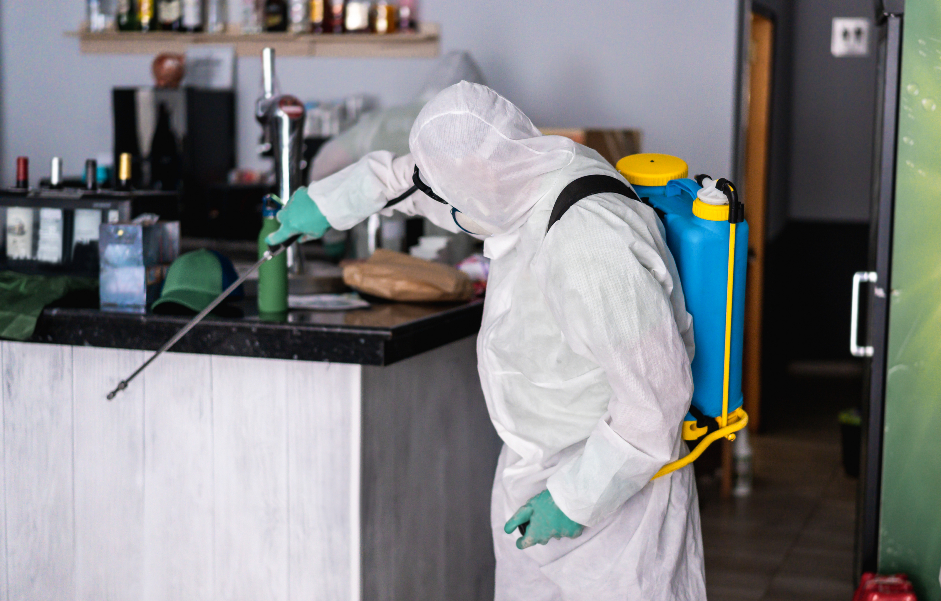 Specialist in wit beschermend pak met nevelspuit vernevelt een bar in een horecagelegenheid.