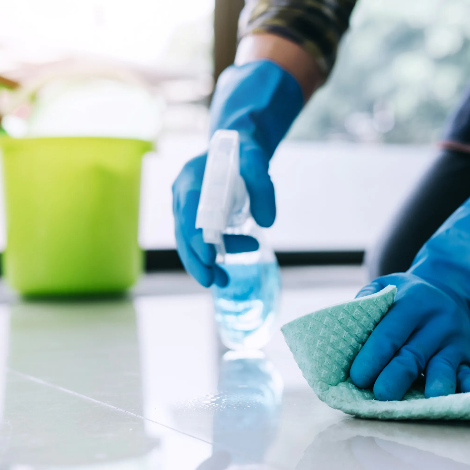 Persoon met werkhandschoenen reinigt een tegelvloer met een microvezeldoek en spray.