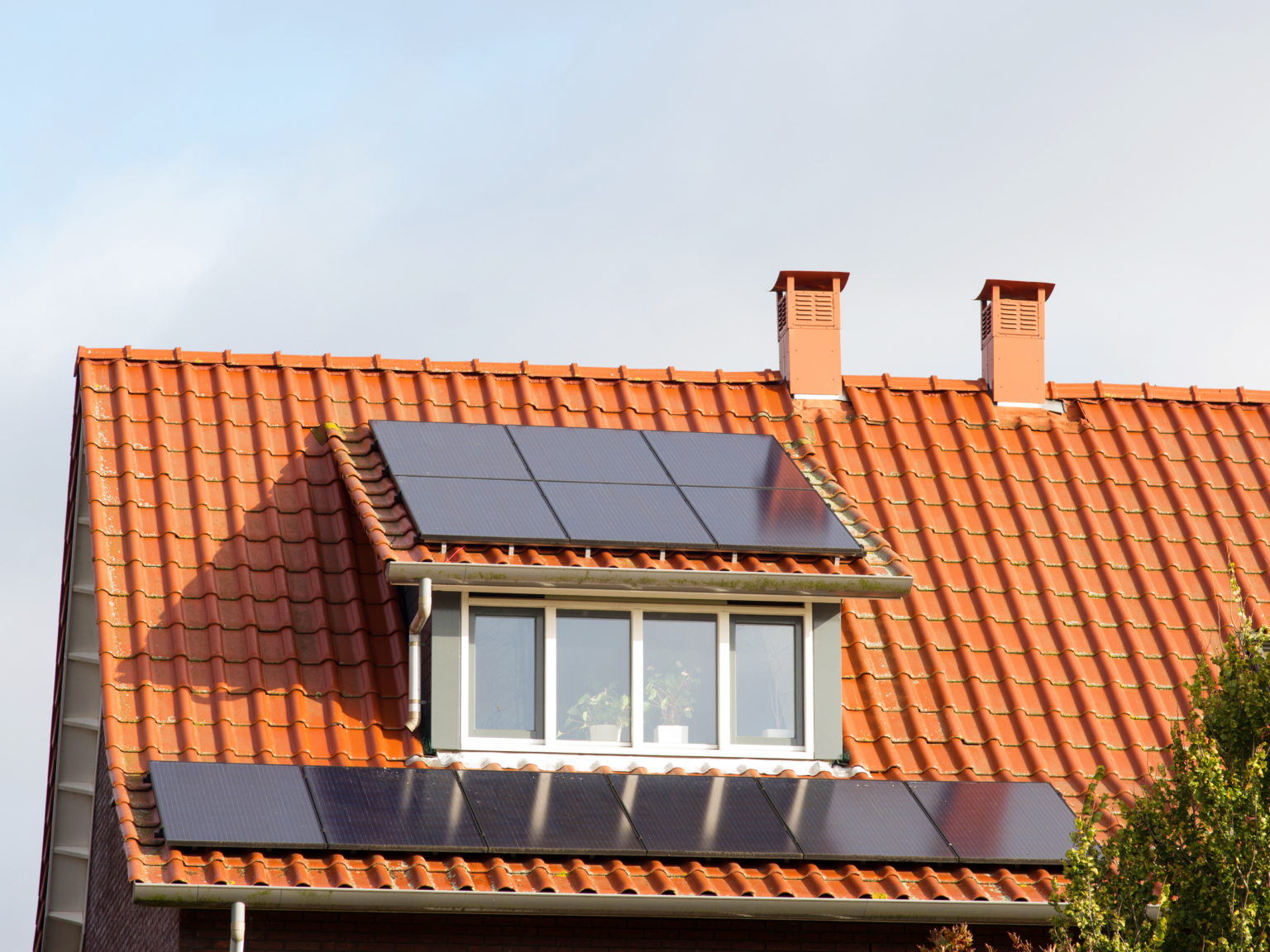 Zonnepanelen gemonteerd op het oranje pannendak van een woning met een dakkapel.
