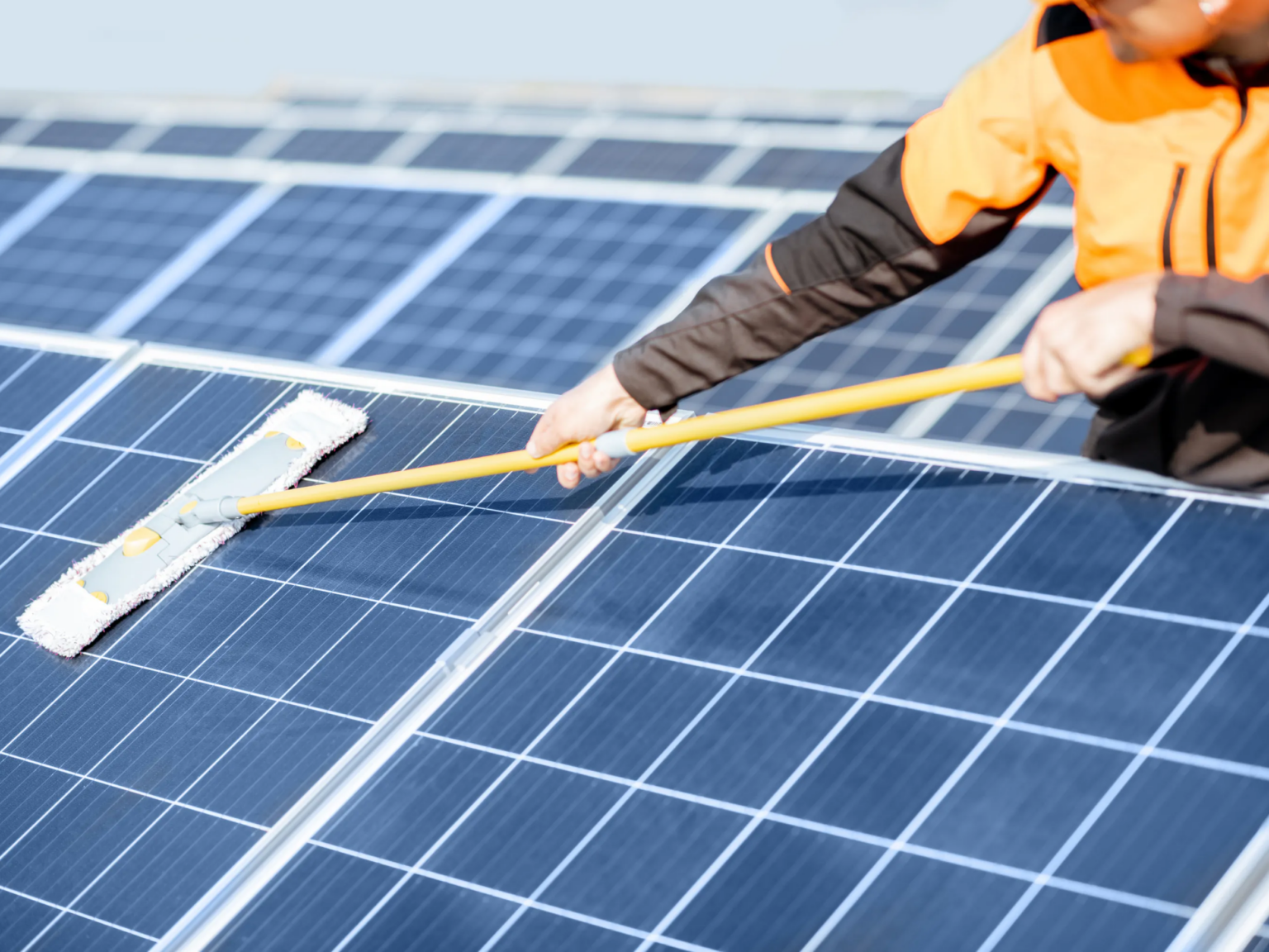 Specialist reinigt zonnepanelen op een dak met een zachte borstel en osmosewater.